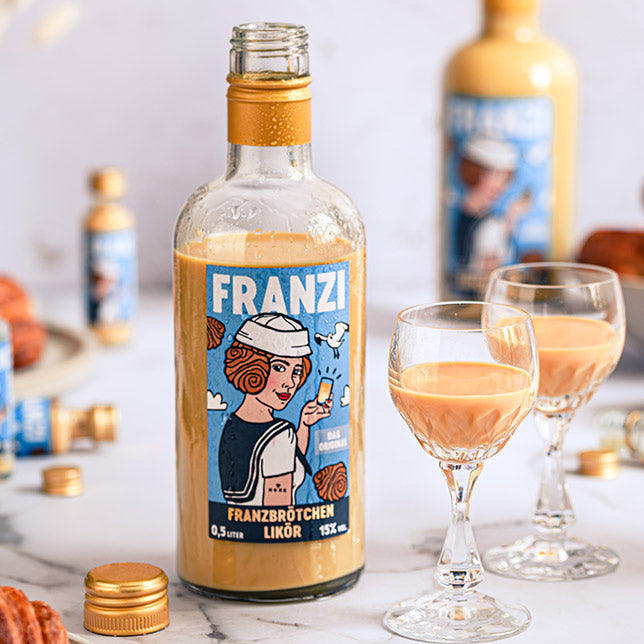 Eine geöffnete Flasche Franzi Franzbrötchen Likör neben zwei mit Likör gefüllten Gläsern
